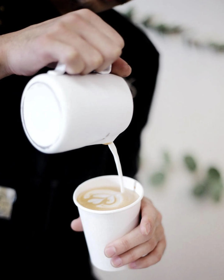 Barista pouring milk into coffee cup